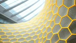 permeable polymer composition, cellular detail, oscillating, photorealistic, modern architectural setting with sweeping angles, highly detailed, rippling motion effect, honeycomb patterning, crystal gray and sunshine yellow, neutral artificial lighting, shot with a 100mm macro lens.